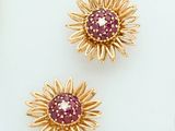 three gold and ruby flower brooches on a white surface