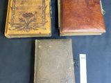 three antique leather bound books are sitting on a blue cloth
