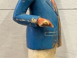 a wooden statue of a man with a blue jacket and white pants
