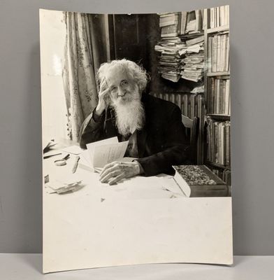 photographie en noir et blanc d'un vieil homme assis à une table avec un livre