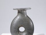 vase gris posé sur un socle blanc, sur fond gris