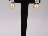 une paire de boucles d'oreilles en perles et diamants posée sur un présentoir noir