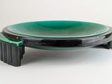 une assiette verte et noire posée sur un support, sur une surface blanche