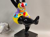 statue d'un clown assis sur un socle noir, sur fond blanc