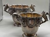 two silver vases sitting on top of a table next to each other