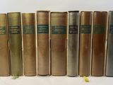 six old books are lined up in a row on a white surface