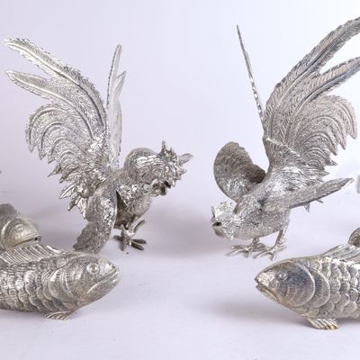 trois figurines en métal argenté représentant des oiseaux et des poissons, posées sur une surface blanche