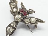 an antique silver broochle with red and white stones on a white surface