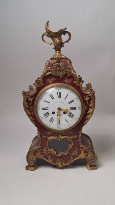 une horloge rouge et dorée posée sur une surface blanche