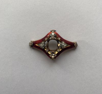 un gros plan d'une broche rouge et dorée posée sur une surface blanche