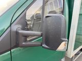 a side view mirror of a green truck with a reflection of a building in the side mirror