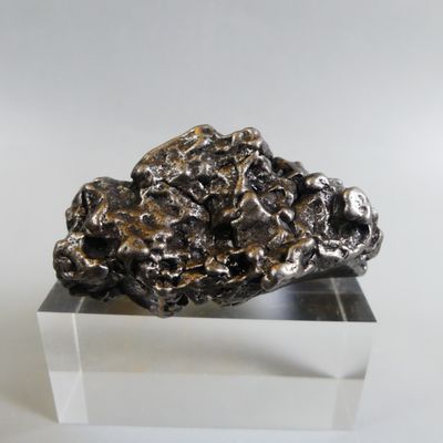 un rocher argenté posé sur un socle transparent, sur une surface blanche