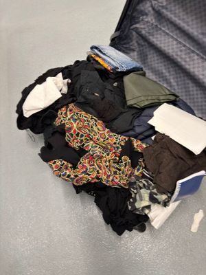 une valise pleine de vêtements et des vêtements par terre