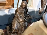 une statue représentant un homme assis sur une chaise à côté d'une lampe