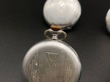 two silver pocket watches sitting next to each other on a black surface