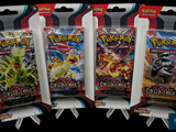 Trois paquets de cartes à collectionner Pokémon sont exposés dans un magasin.