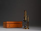 un vieux microscope en laiton posé sur une table, dans un coffret en bois