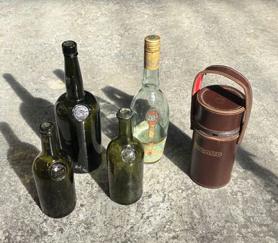 several empty wine bottles and a leather case sitting on a concrete surface
