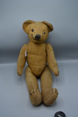 un ours en peluche marron assis sur une surface blanche, à côté d'une pièce de monnaie