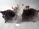 two silver vases with statues on them on a table