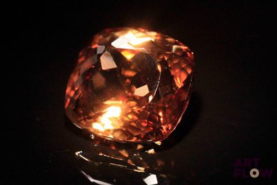 a close up of a fancy orange diamond on a black surface