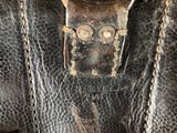 an old brown leather bag with a metal handle on a white surface