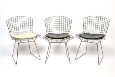 three metal chairs with black cushions on them against a white background