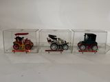 three toy cars in a display case on a white surface