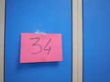 un post-it rose collé sur une porte bleue, sur lequel est inscrit le chiffre 34