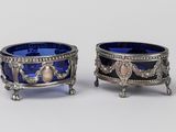 une paire de bols en verre argenté et bleu, posés sur des socles, sur une surface blanche