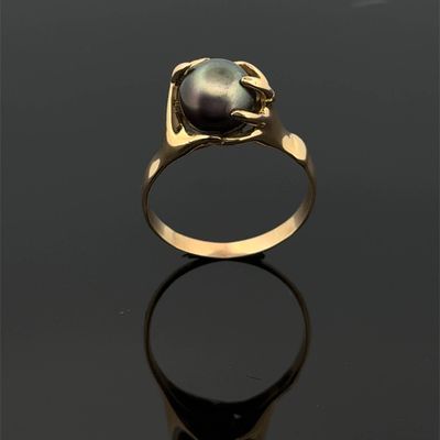 a gold ring with a black pearl on a black surface