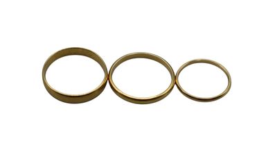 three gold wedding rings sitting side by side on a white surface