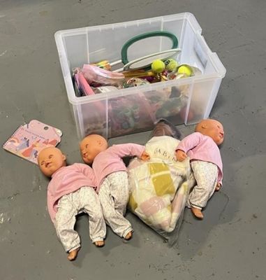 trois poupées posées par terre à côté d'un bac en plastique