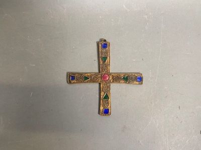 a gold cross with colorful stones on it on a white surface