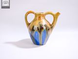 un vase bleu et jaune posé sur une surface blanche