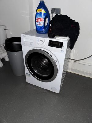 une machine à laver sur laquelle est posée une bouteille de lessive, à côté d'une poubelle