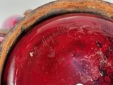 an old red vase with a tag on it sitting on a table