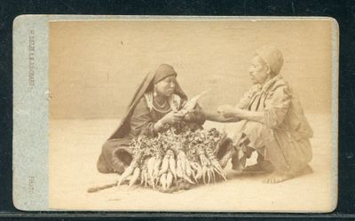 une vieille photo montrant deux femmes assises à côté d'un tas de légumes