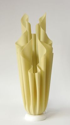 un vase blanc contenant du papier jaune, posé sur une surface blanche