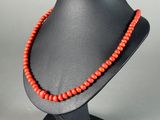 a red beaded necklace on a black mannequin stand