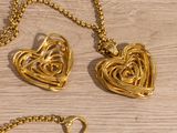 two gold heart shaped pendants on a gold chain on a wooden surface