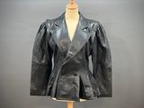 une veste en cuir noir posée sur un mannequin, devant un fond gris