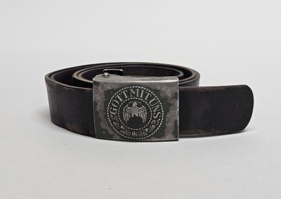 la ceinture est noire et comporte une boucle métallique ornée d'un emblème