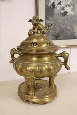a large brass incense pot on a stand with a picture on the wall in the background