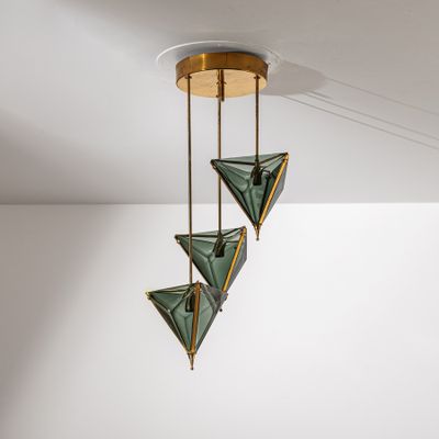 un gros plan sur un plafonnier composé de trois triangles en verre vert suspendus au plafond