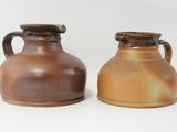 deux vases marron munis d'anses, posés côte à côte sur une surface blanche