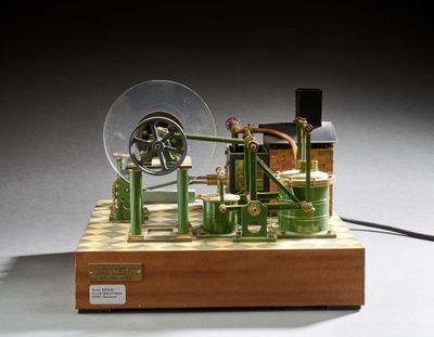 une petite maquette de machine à vapeur posée sur un socle en bois