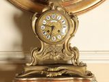 une horloge en or posée sur un socle en marbre devant un miroir