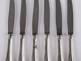 six knives are lined up on a white surface