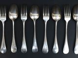 six forks and six spoons are lined up on a black surface